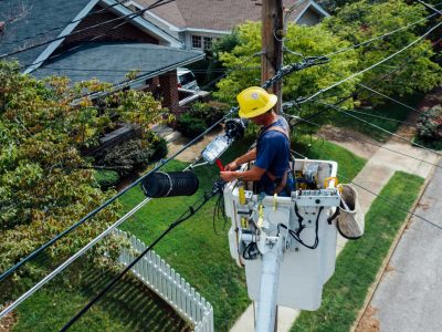 Electrician in a bucket lift repairing power lines from a utility pole in a suburban neighborhood.